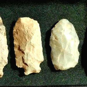 May include: Four arrowheads made of different types of stone. The arrowheads are all different shapes and sizes. They are displayed on a green felt background.