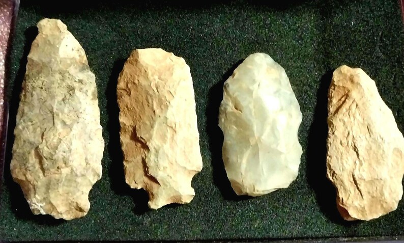 May include: Four arrowheads made of different types of stone. The arrowheads are all different shapes and sizes. They are displayed on a green felt background.