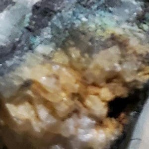 May include: Close-up of a textured, multi-colored surface with shades of blue, green, yellow, and white. The surface has a rough, uneven texture and appears to be made of natural materials.