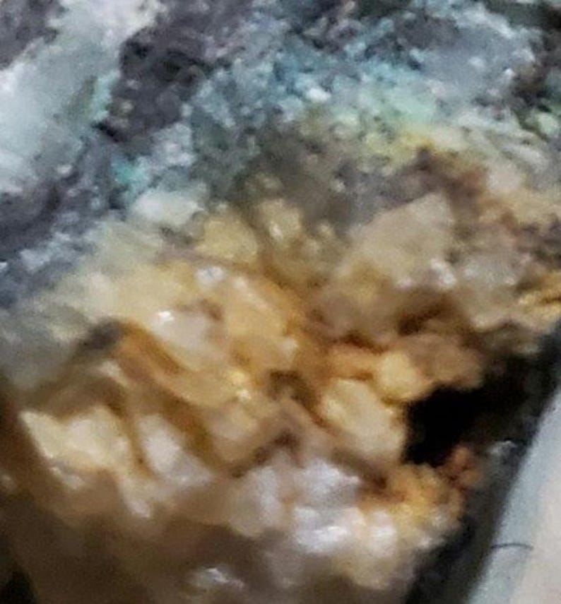 May include: Close-up of a textured, multi-colored surface with shades of blue, green, yellow, and white. The surface has a rough, uneven texture and appears to be made of natural materials.
