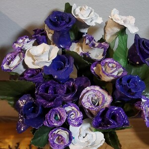 May include: A bouquet of purple and white paper roses in a clear glass vase. The roses are arranged in a cluster and have a textured, paper-like appearance.