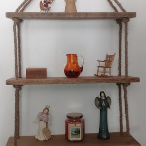 May include: Three wooden shelves with rope hangers, decorated with figurines, a pitcher, a candle, and a sign that reads "From the Ranch to You".