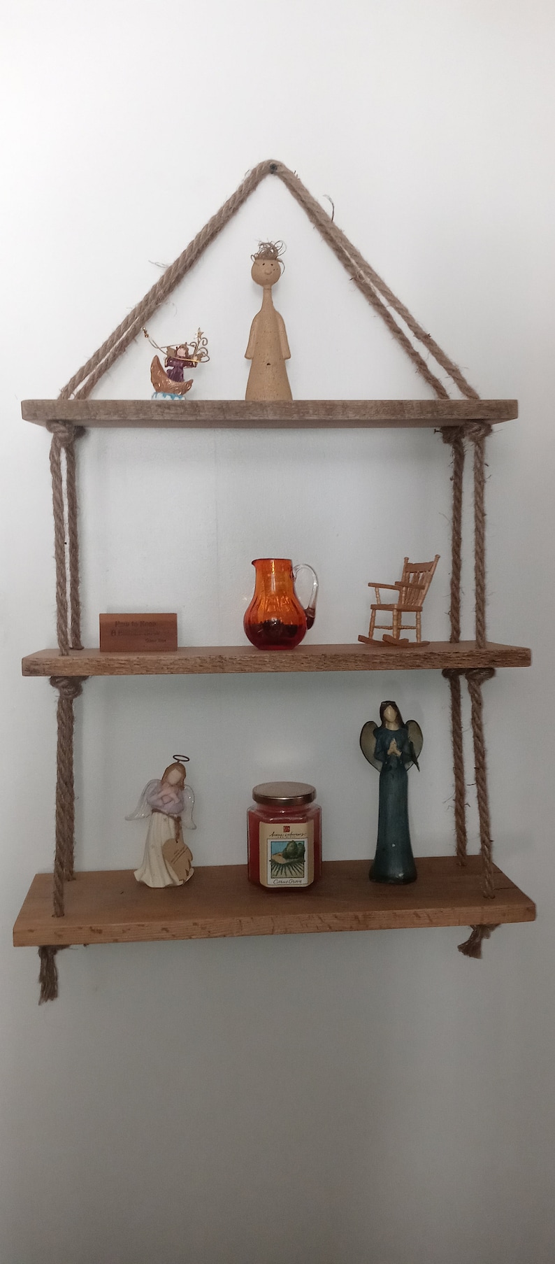 May include: Three wooden shelves with rope hangers, decorated with figurines, a pitcher, a candle, and a sign that reads "From the Ranch to You".