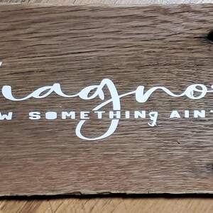 May include: A rectangular wooden sign with the words "undiagnosed BUT I KNOW SOMETHING AIN'T RIGHT" in white script. The sign is made of weathered wood with visible grain and knots, and has a rustic appearance.