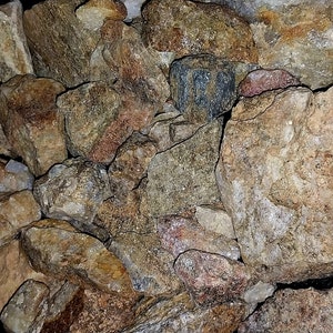 May include: A collection of various rough-cut rocks and stones. The stones display a range of colors, including tan, brown, gray, and hints of red. The image showcases the natural textures and irregular shapes of the rocks.