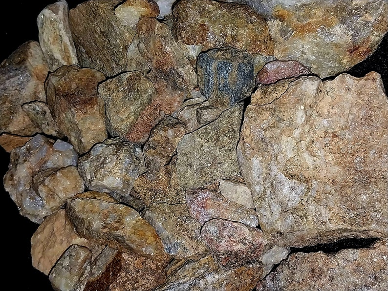 May include: A collection of various rough-cut rocks and stones. The stones display a range of colors, including tan, brown, gray, and hints of red. The image showcases the natural textures and irregular shapes of the rocks.