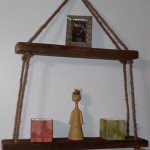 May include: A rustic wooden shelf with rope hangers, featuring a small framed picture, a ceramic figurine, and two square containers.