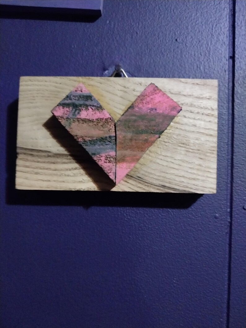 May include: A wooden plaque with a heart-shaped design made of pink and gray textured paper. The heart is centered on the plaque.