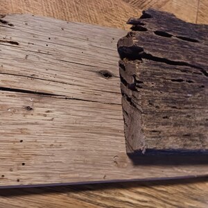May include: Two pieces of weathered wood with a rough, uneven texture. The wood is a light brown color with dark brown spots and holes. The wood appears to be old and worn.