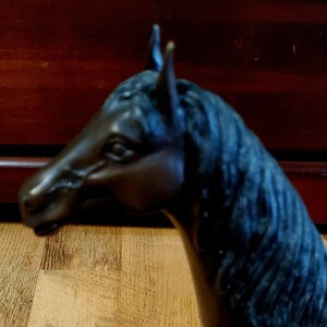 May include: A bronze-colored horse head sculpture. The sculpture features a detailed mane and a realistic depiction of the horse's facial features. The horse head is positioned in profile, showcasing its elegant form.