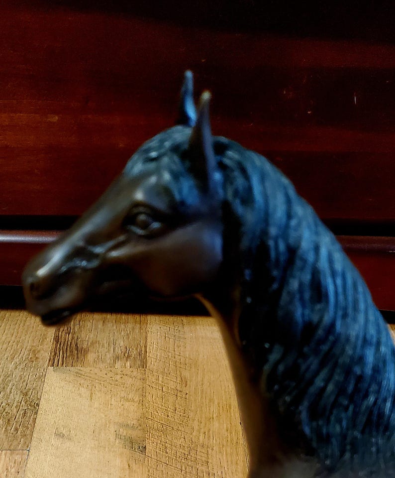 May include: A bronze-colored horse head sculpture. The sculpture features a detailed mane and a realistic depiction of the horse's facial features. The horse head is positioned in profile, showcasing its elegant form.