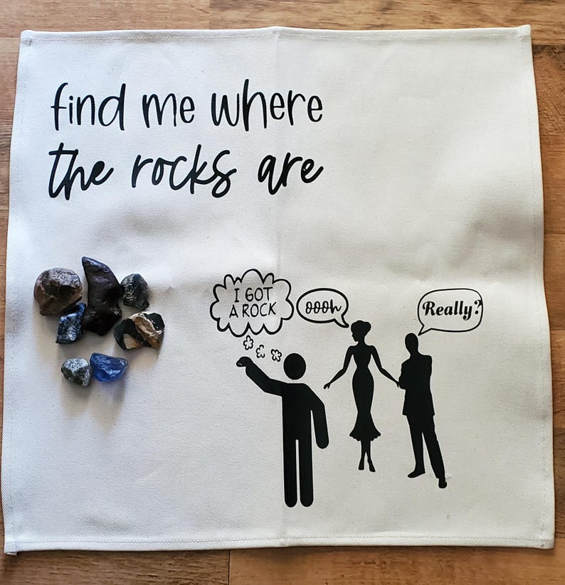 May include: A white cloth with the text "find me where the rocks are" and a cartoon illustration. The illustration includes a person pointing at a group of rocks, speech bubbles, and silhouettes of people. Various rocks are displayed.