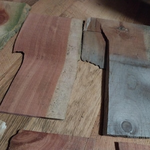 May include: A collection of irregularly shaped wooden planks in various shades of brown, red, and gray. The planks have visible wood grain and knots, suggesting a natural, rustic aesthetic. Some pieces have a rough, unfinished edge.