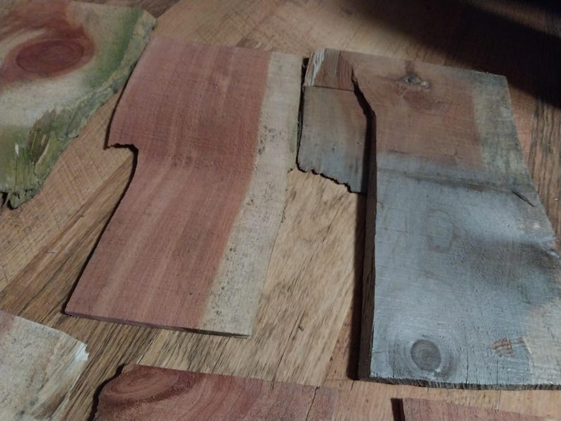 May include: A collection of irregularly shaped wooden planks in various shades of brown, red, and gray. The planks have visible wood grain and knots, suggesting a natural, rustic aesthetic. Some pieces have a rough, unfinished edge.