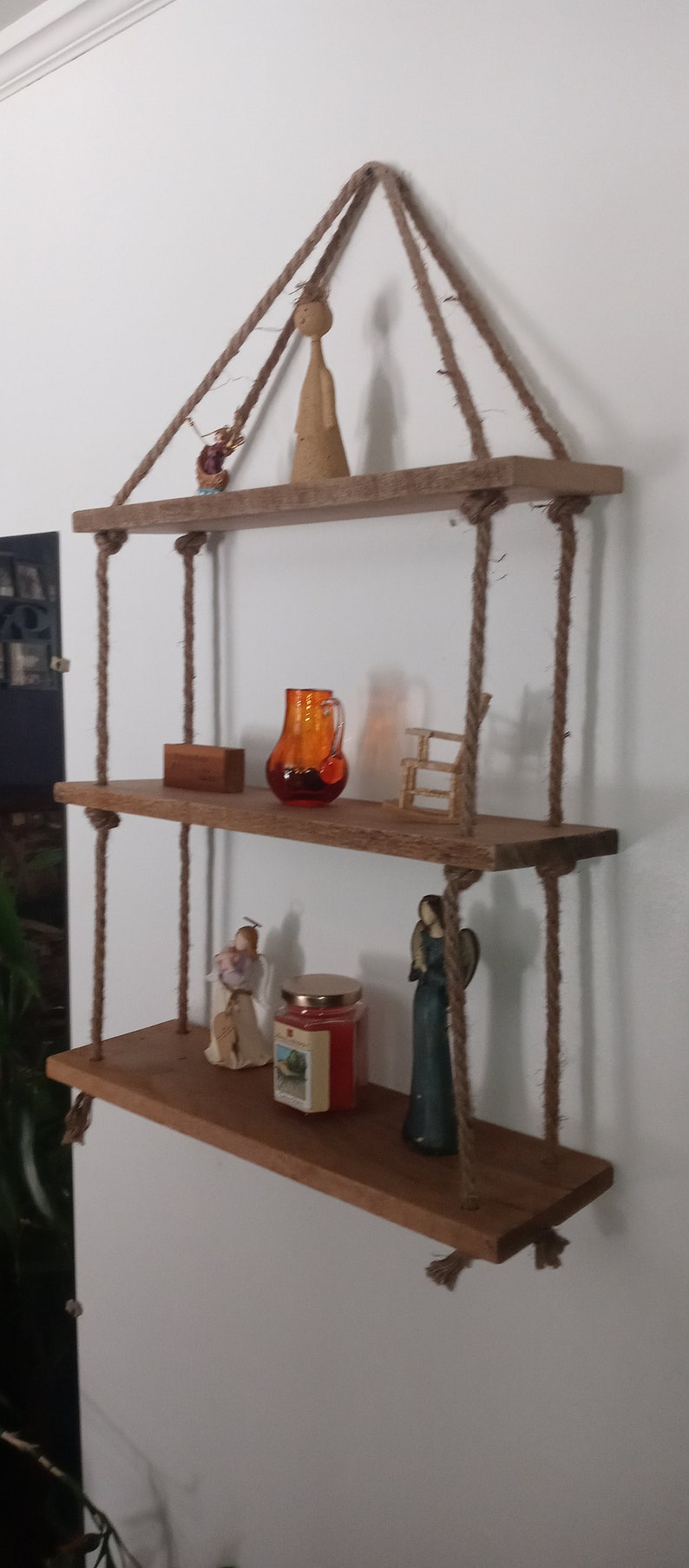 May include: Three wooden shelves hanging from the ceiling with rope. The shelves are decorated with small figurines, a glass pitcher, and a candle.