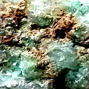May include: A close-up of a green and brown rock with a rough, textured surface. The rock has a variety of shades of green and brown, and the texture is very rough and uneven.
