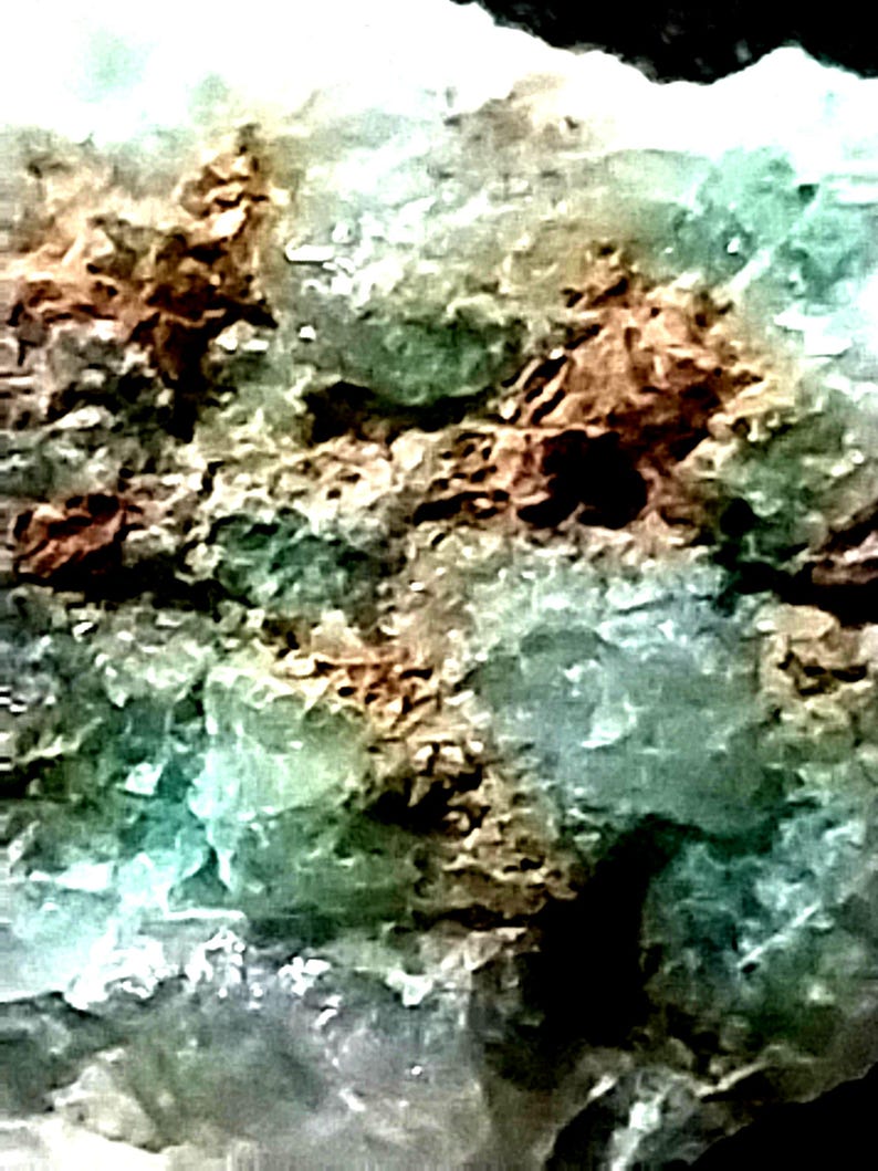 May include: A close-up of a green and brown rock with a rough, textured surface. The rock has a variety of shades of green and brown, and the texture is very rough and uneven.