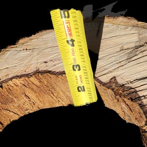 K&ouml;nnte beinhalten: Nahaufnahme eines gro&szlig;en, runden St&uuml;ckes Holz mit einem gelben Ma&szlig;band in der Mitte. Das Holz hat eine nat&uuml;rliche, raue Textur und eine hellbraune Farbe.