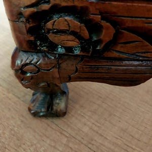 May include: Close-up of a carved wooden furniture piece. The dark brown wood features intricate floral and leaf designs, with a detailed carved leg. The wood has a glossy finish, and the piece appears to be antique.
