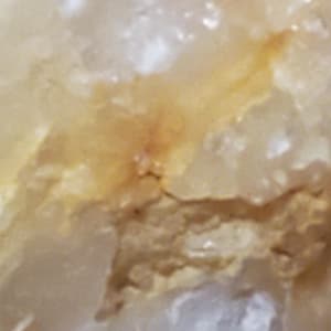 May include: Close-up of a natural stone with a mix of white, beige, and golden-yellow hues. The surface has a rough, textured appearance with subtle variations in color and small, irregular shapes.