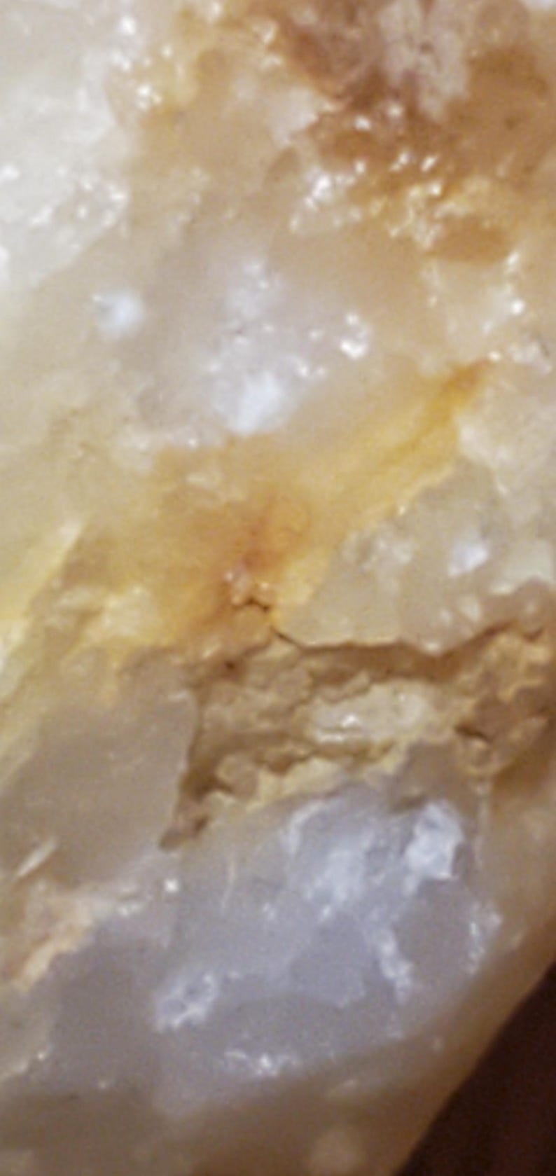 May include: Close-up of a natural stone with a mix of white, beige, and golden-yellow hues. The surface has a rough, textured appearance with subtle variations in color and small, irregular shapes.