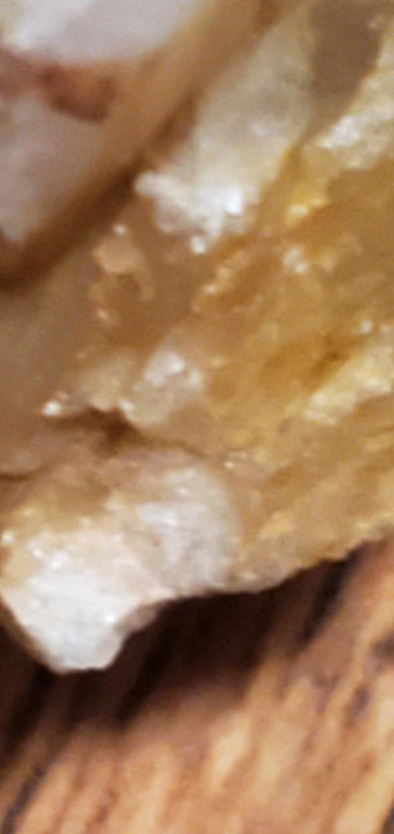 May include: Close-up of a rough, textured, light brown surface with white and tan highlights. The surface appears to be a natural material, possibly a rock or mineral, with a slightly uneven texture.