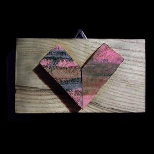 May include: A wooden heart-shaped ornament with pink and black stripes. The heart is made of two pieces of wood that are joined together.
