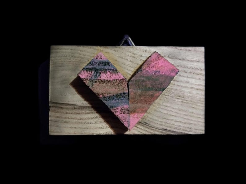 May include: A wooden heart-shaped ornament with pink and black stripes. The heart is made of two pieces of wood that are joined together.