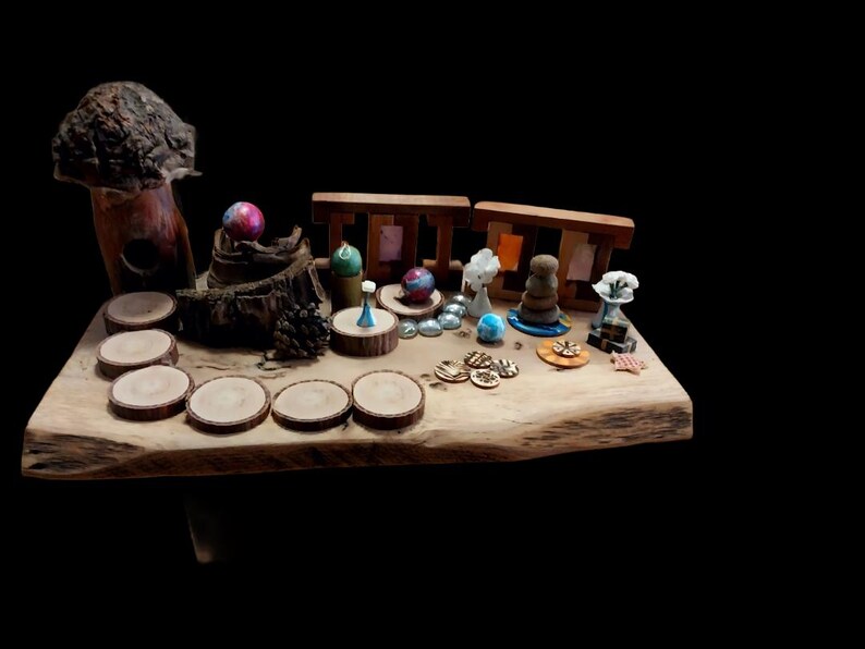 May include: A rustic wooden table displays a collection of miniature decorative items. The arrangement includes wooden coasters, small sculptures, colorful spheres, and a wooden structure, all set against a black background.