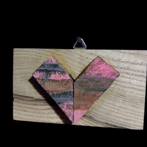 May include: A wooden heart-shaped wall hanging with a pink and purple painted design.