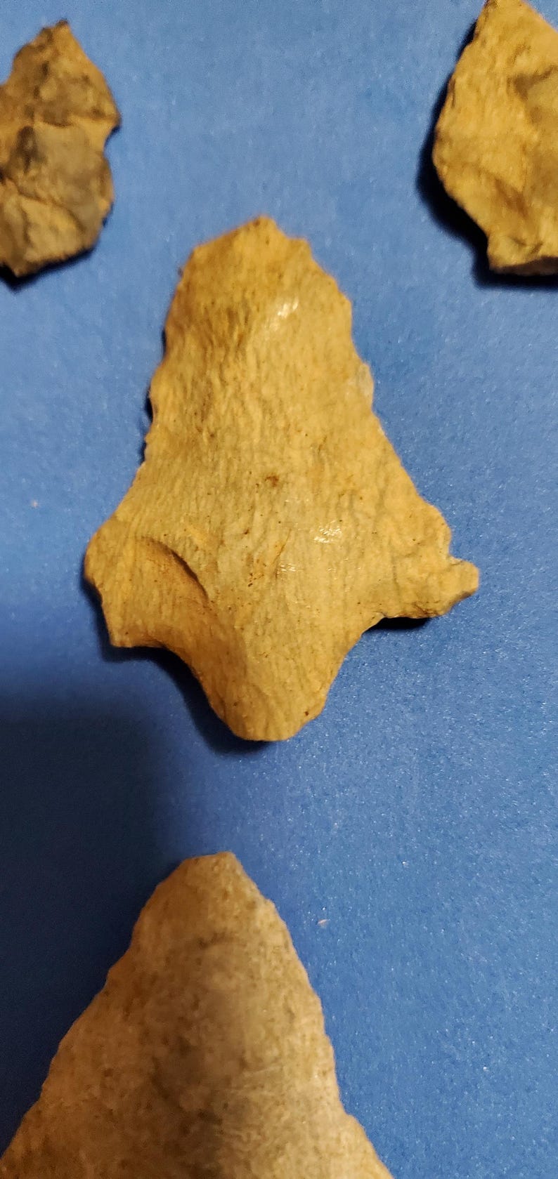 Pode incluir: Uma cole&ccedil;&atilde;o de antigas pontas de flecha e ferramentas de pedra de cor bege, cada uma com formas e texturas &uacute;nicas. Os artefatos s&atilde;o exibidos em um fundo azul, mostrando sua import&acirc;ncia hist&oacute;rica.