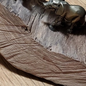 May include: Two small, bronze-colored elephant figurines on a piece of wood. One elephant is standing upright, while the other is in a walking pose. The wood has a textured, brown surface, and the background is a light-colored wooden floor.