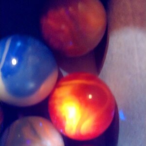 May include: A collection of colorful, spherical objects, possibly marbles or decorative stones, in shades of red, orange, blue, and brown. The objects have a glossy, reflective surface and are arranged in a container.