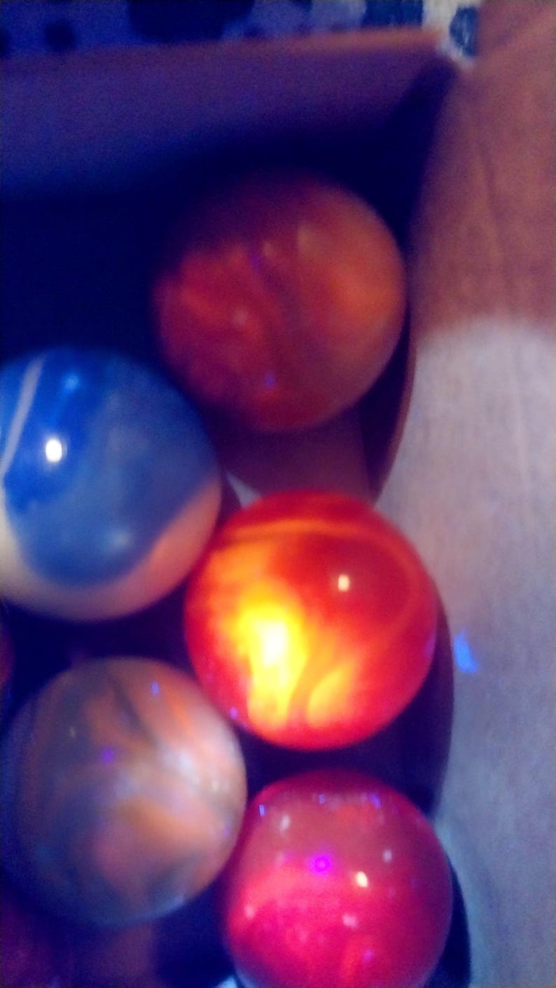 May include: A collection of colorful, spherical objects, possibly marbles or decorative stones, in shades of red, orange, blue, and brown. The objects have a glossy, reflective surface and are arranged in a container.