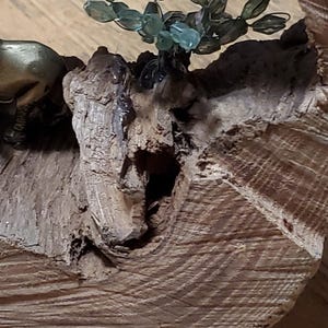 May include: A decorative wooden sculpture featuring a small bronze animal figure and a cluster of green glass beads resembling a plant. The sculpture is mounted on a piece of textured, light brown wood.