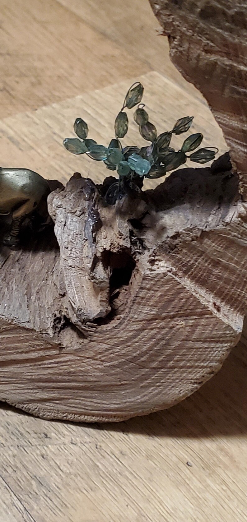 May include: A decorative wooden sculpture featuring a small bronze animal figure and a cluster of green glass beads resembling a plant. The sculpture is mounted on a piece of textured, light brown wood.
