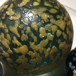 Op de afbeelding: Een groene glazen knikker met gele en oranje vlekken.