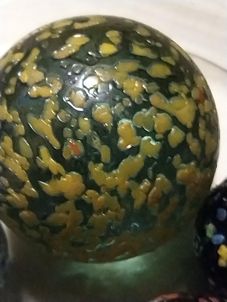 Op de afbeelding: Een groene glazen knikker met gele en oranje vlekken.
