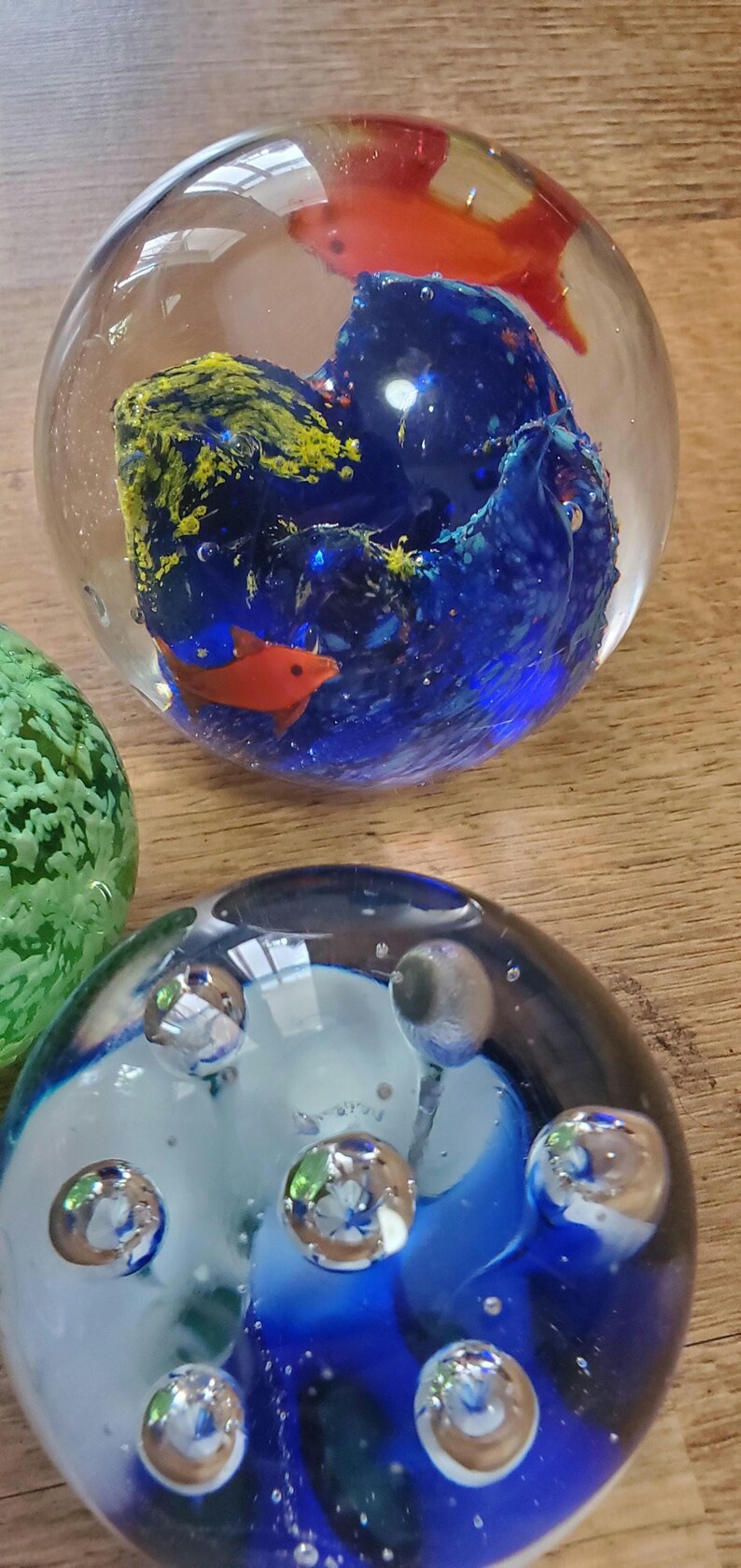 May include: Glass paperweights with underwater designs. One has a blue and yellow coral reef with orange fish. Another features blue and white swirls with bubbles. Decorative glass art pieces.