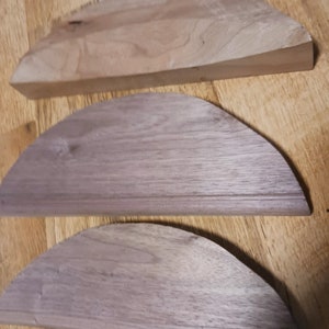 May include: Three wooden half-circle shapes, the top one is flat and the bottom two are curved. The wood is a light brown color.