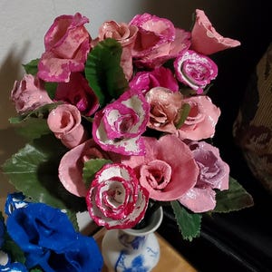 May include: A bouquet of pink and white paper roses in a blue and white porcelain vase. The roses are arranged in a cluster and have a delicate, handmade appearance.