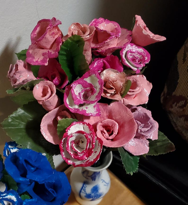 May include: A bouquet of pink and white paper roses in a blue and white porcelain vase. The roses are arranged in a cluster and have a delicate, handmade appearance.