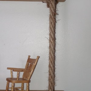 May include: Two wooden shelves hanging from the ceiling with thick brown rope. The top shelf has a small wooden rocking chair on it. The bottom shelf has a small angel figurine on it.