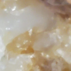 May include: Close-up of a textured, off-white surface with hints of brown and yellow. The image has a soft, diffused focus, suggesting a natural or organic material.