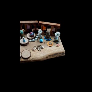 May include: A wooden display featuring miniature decorative items. Includes small sculptures, wooden rounds, and colorful glass beads. The items are arranged on a natural wood surface, with a dark background.