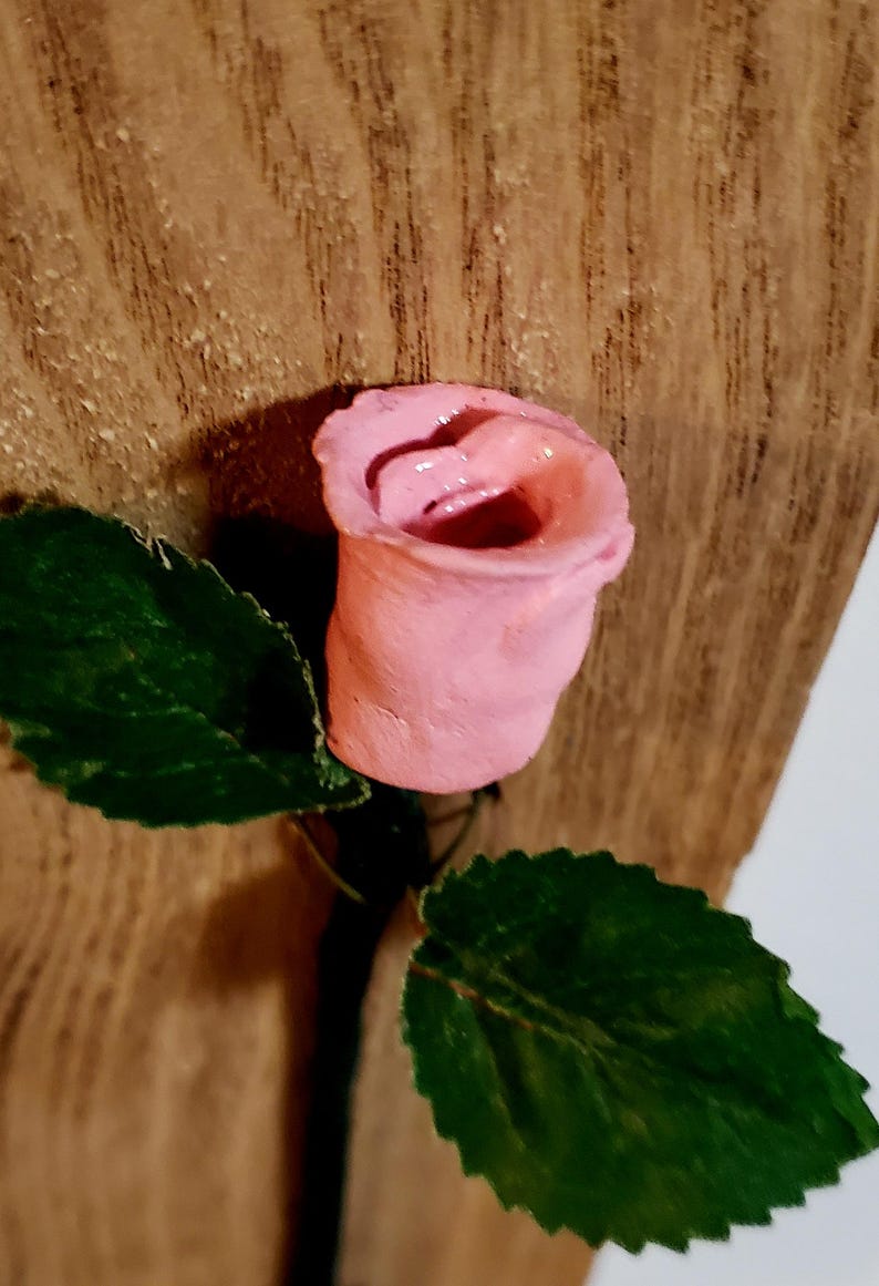 May include: A pink ceramic rose with green leaves attached to a wooden surface.