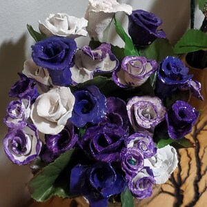 May include: A bouquet of paper roses in shades of white and purple. The roses are arranged in a vase and have a vintage, rustic look.