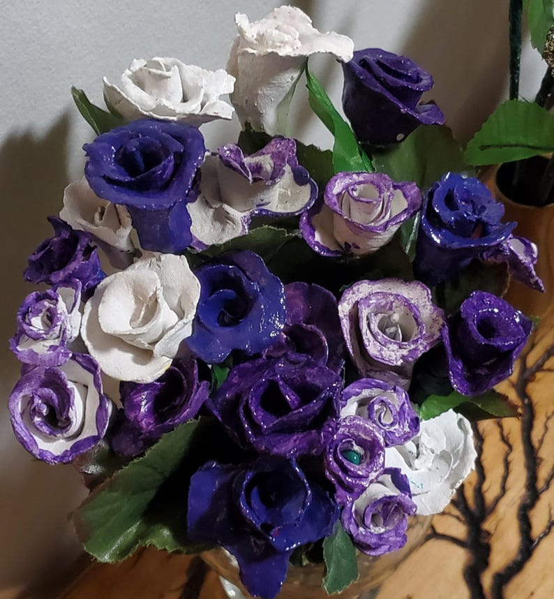 May include: A bouquet of paper roses in shades of white and purple. The roses are arranged in a vase and have a vintage, rustic look.