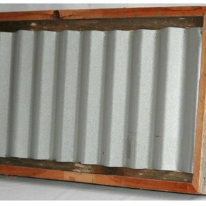 May include: A rectangular wooden frame with a corrugated metal insert. The frame is made of light brown wood with a darker brown trim around the metal. The metal is silver and has a ridged texture.
