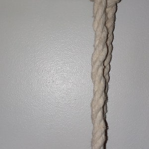 May include: A white rope is tied to a wooden shelf. The rope is knotted and hangs down from the shelf.
